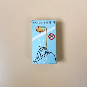 May include: A vintage box with the text "APPENDI BORSETTE" and a graphic of a purse hanger. The box is light blue with a gold-colored metal purse hanger illustration. The hanger has a rectangular top and a curved hook.