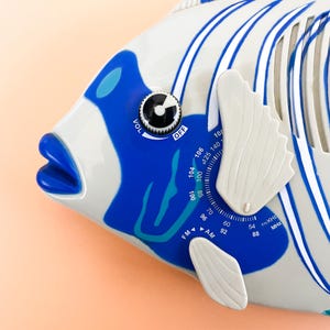 May include: A blue and white fish-shaped radio with a dial that reads "FM", "AM", and numbers from 54 to 140. The radio has a volume knob and an "OFF" switch.