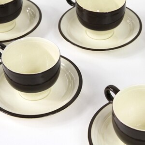 Peut inclure: Ensemble de six tasses à thé et soucoupes blanches et brunes. Les tasses et les soucoupes ont une bande noire autour du bord.