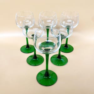 Peut inclure: Ensemble de six verres à vin en verre transparent avec des tiges et des bases vertes. Les verres sont disposés en cercle, les tiges pointant vers l'extérieur.