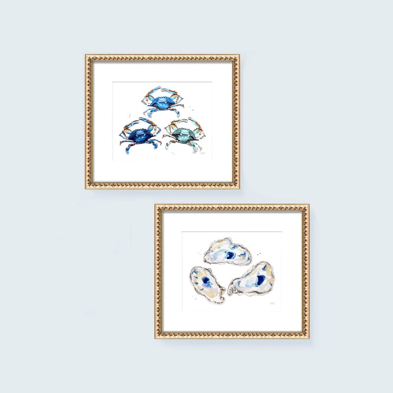 May include: Two framed watercolor paintings, one with blue crabs and the other with blue and white oysters. Both paintings have a gold frame.