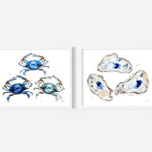 May include: Two framed watercolor paintings. One features three blue crabs with orange claws. The other features three oyster shells with blue and white interiors.