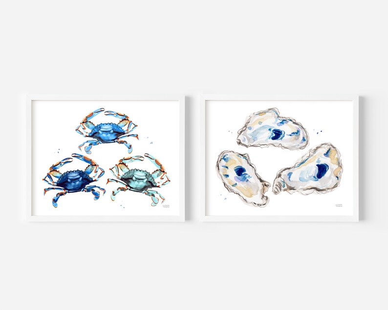 May include: Two framed watercolor paintings. One features three blue crabs with orange claws. The other features three oyster shells with blue and white interiors.