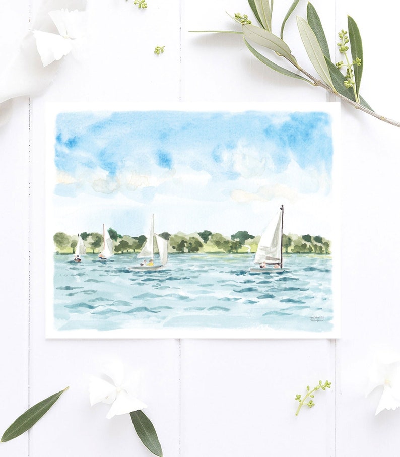 May include: Watercolor painting of sailboats on a lake under a blue sky with clouds. The artwork features several white sailboats with their sails up, sailing on blue water. Green trees line the distant shore. The painting is on white paper.