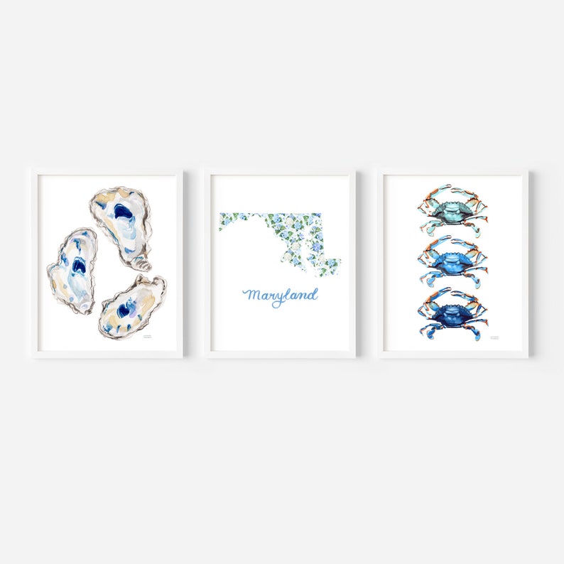 May include: A set of three framed wall art prints. The left print shows three watercolor oysters. The center print features a floral-patterned map of Maryland with the text Maryland below. The right print displays three blue crabs in a vertical row.
