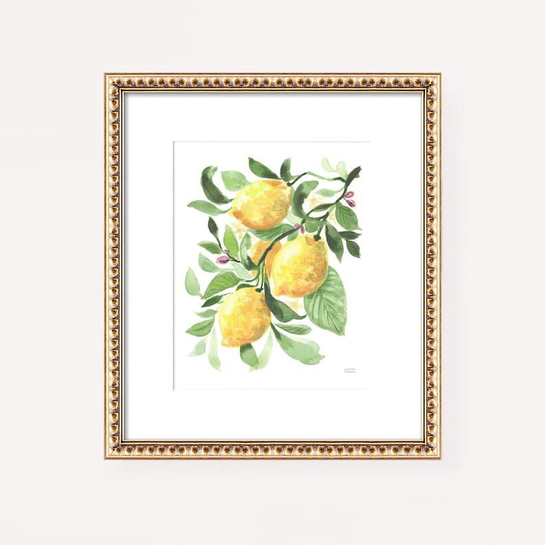 May include: Watercolor painting of lemons on a branch with green leaves and small pink flowers. The artwork is framed in a gold-colored frame with a white mat. The painting has a bright and cheerful aesthetic.