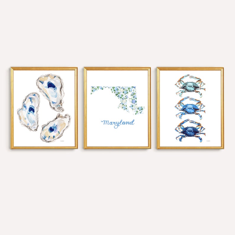 May include: A set of three framed wall art prints. The left print shows three watercolor oysters. The center print features a floral-patterned map of Maryland with the text Maryland below. The right print displays three blue crabs in a vertical row.