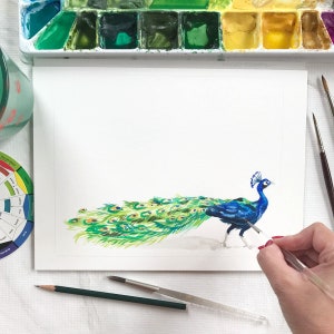 May include: A watercolor painting of a peacock with a blue body and green and gold tail feathers. The artist is using a paintbrush to add details to the painting.