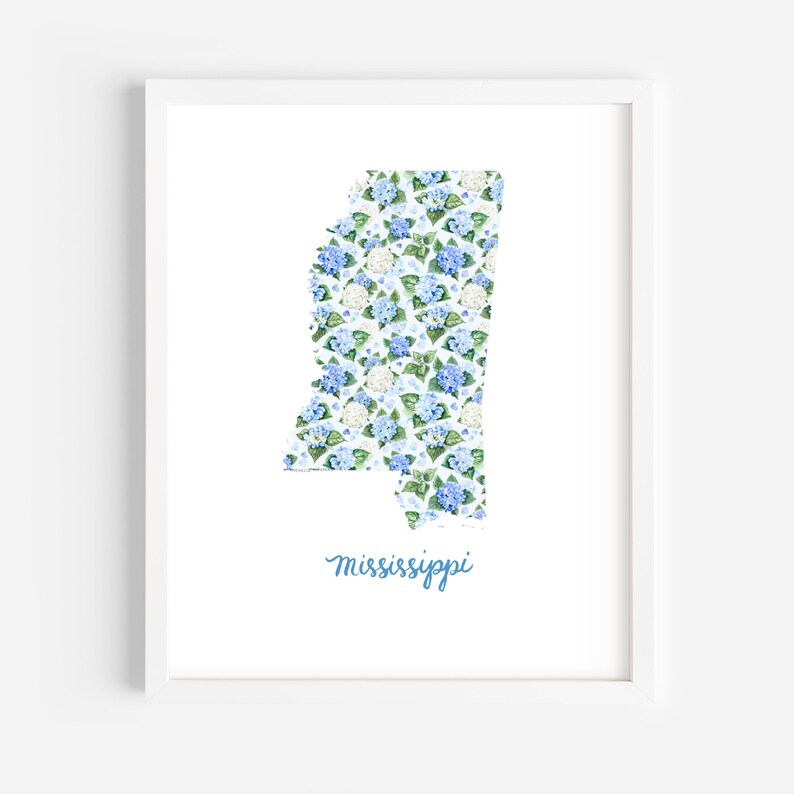 May include: A framed art print featuring the state of Mississippi, filled with a floral pattern of blue and white hydrangeas. The word "Mississippi" is written in a cursive font below the state outline. The artwork is set against a white background.