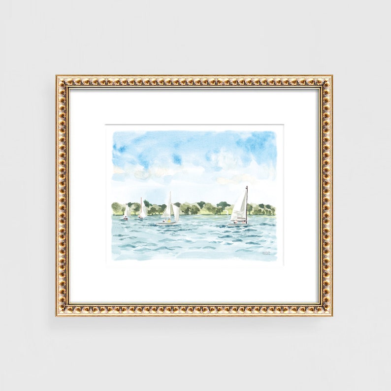 May include: Watercolor painting of sailboats on a blue lake under a light blue sky. The artwork is framed in a gold beaded frame with a white mat. Green trees line the horizon in the background.