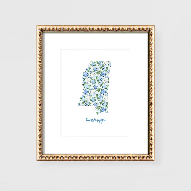 May include: Framed art print featuring the state of Mississippi filled with a floral pattern of blue and white flowers. The word "Mississippi" is written in cursive below the state outline. The frame is gold with a decorative edge.