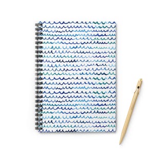 May include: A spiral-bound notebook with a white cover featuring a pattern of blue and teal wavy lines. A gold pen rests beside the notebook. The notebook's spiral binding is black.