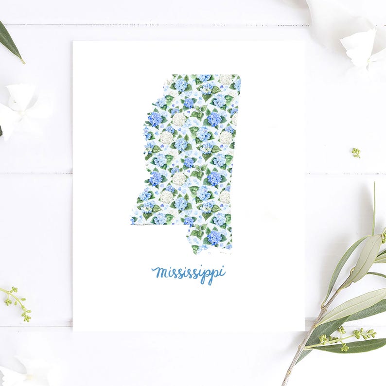 May include: A white print featuring the state of Mississippi filled with a blue and white floral pattern. The word "Mississippi" is written in cursive script in a light blue color at the bottom of the print.