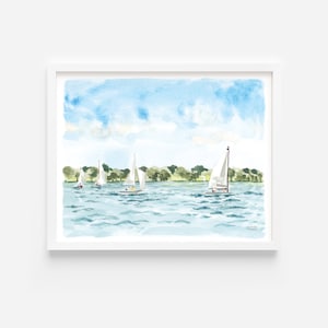 May include: Watercolor painting of sailboats on a lake under a blue sky with fluffy clouds. The artwork features several white sailboats with their sails up, sailing on the blue water. Green trees line the distant shore, and the painting is framed in a white border.