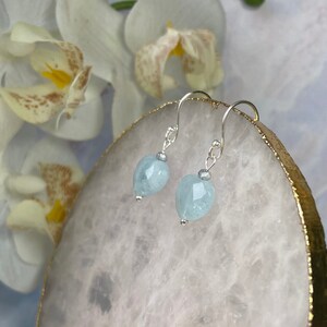May include: A pair of silver dangle earrings with light blue heart-shaped aquamarine stones.