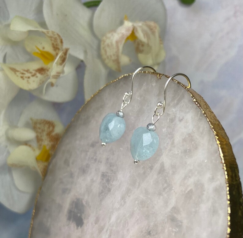 May include: A pair of silver dangle earrings with light blue heart-shaped aquamarine stones.