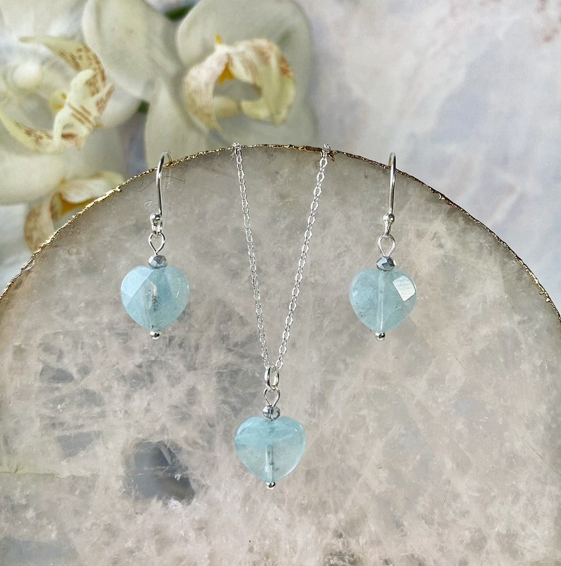 May include: A silver necklace and earrings set with light blue heart-shaped aquamarine stones.