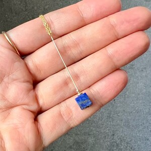 Puede incluir: Un collar de cadena dorada con un colgante cuadrado de lapisl&aacute;zuli.