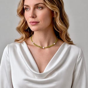 May include: A delicate choker necklace featuring a strand of small, faceted olive-green beads interspersed with evenly spaced, smooth white pearls. The necklace rests against the neck, showcasing a simple, refined design with a polished finish.