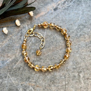 May include: A gold bracelet with a chain extender, featuring faceted, light brown gemstone beads.