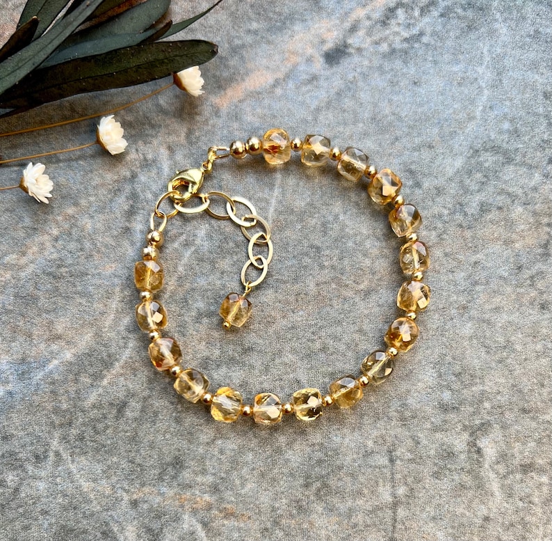 May include: A gold bracelet with a chain extender, featuring faceted, light brown gemstone beads.