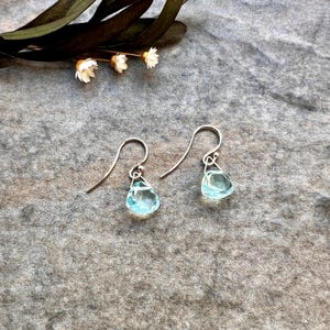 May include: A pair of silver teardrop earrings with light blue gemstone accents.