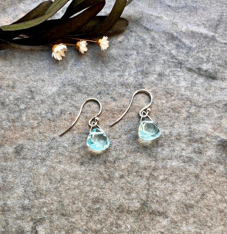 May include: A pair of silver teardrop earrings with light blue gemstone accents.