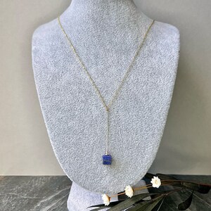 Puede incluir: Un collar de cadena dorada con un largo y delgado colgante que presenta una piedra cuadrada de lapisl&aacute;zuli azul oscuro.