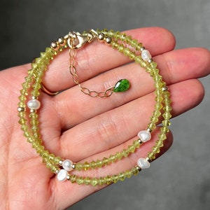 May include: A delicate bracelet featuring small, faceted lime-green peridot beads interspersed with white freshwater pearls and gold-toned metal spacers. The piece includes a gold-toned chain extender finished with a single, small, teardrop-shaped green gemstone charm.