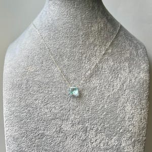 May include: A silver chain necklace with a light blue gemstone pendant.