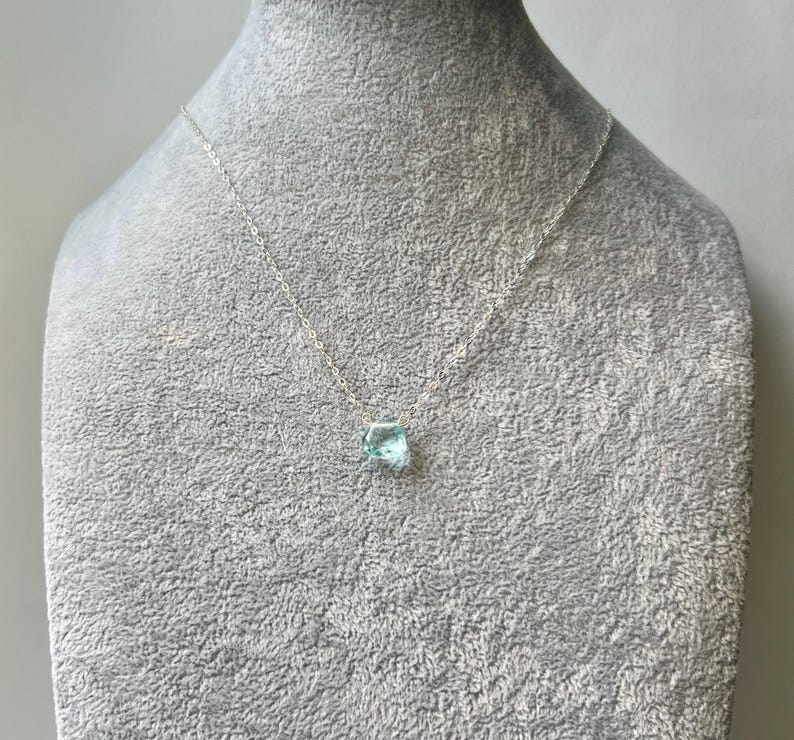 May include: A silver chain necklace with a light blue gemstone pendant.