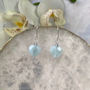 May include: A pair of silver dangle earrings with light blue heart-shaped aquamarine stones.