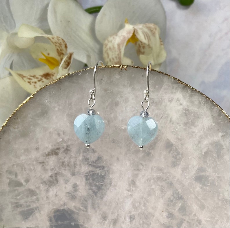 May include: A pair of silver dangle earrings with light blue heart-shaped aquamarine stones.