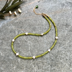 Könnte beinhalten: Eine Perlenkette mit kleinen, facettierten, lindgrünen Kristallen, durchsetzt mit unregelmäßigen weißen Süßwasserperlen und winzigen goldfarbenen Metallzwischenstücken, ergänzt durch eine goldfarbene Kette und einen kleinen grünen Tropfenanhänger.