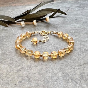May include: A gold bracelet with a chain closure and a row of faceted, light amber-colored beads.
