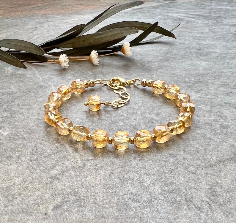 May include: A gold bracelet with a chain closure and a row of faceted, light amber-colored beads.