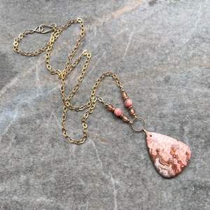 May include: A gold chain necklace with pink and brown beads and a large pink and brown agate pendant.