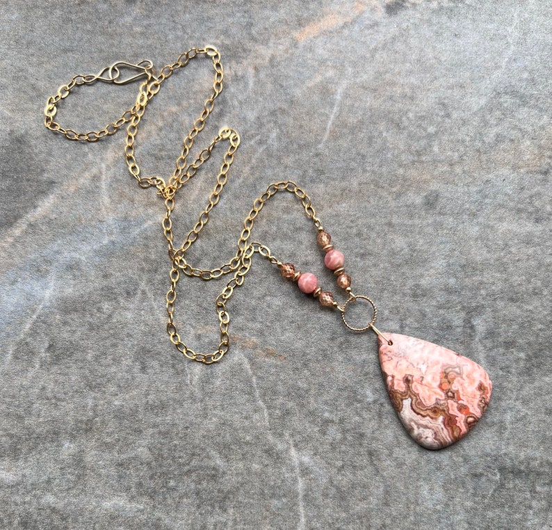 May include: A gold chain necklace with pink and brown beads and a large pink and brown agate pendant.