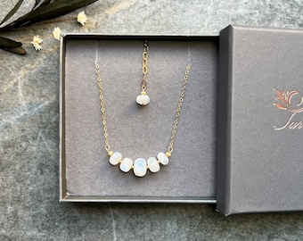 May include: A gold chain necklace with a row of white moonstone beads in a gray gift box. The necklace has a small moonstone pendant.
