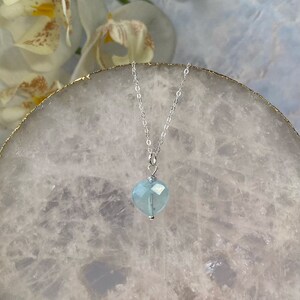 May include: A delicate silver chain necklace with a light blue heart-shaped pendant.
