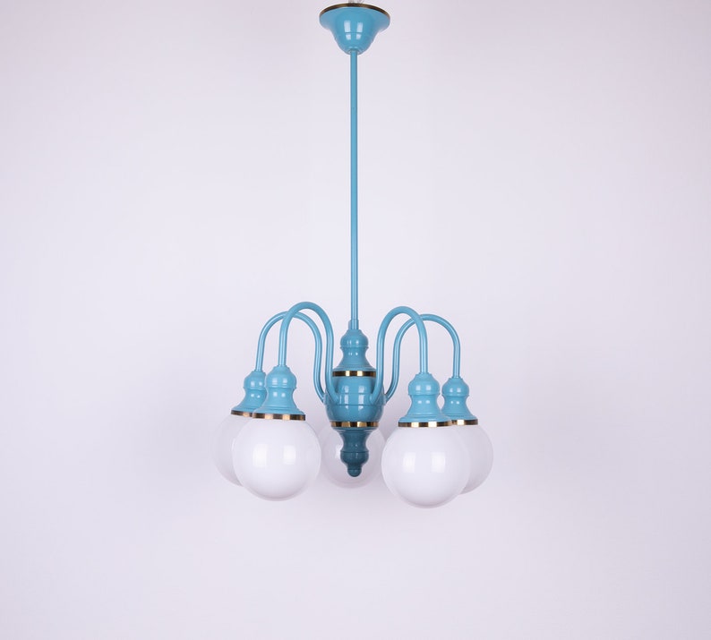 May include: A light blue chandelier with six white globe-shaped light bulbs. The chandelier has a gold trim around the base of each bulb.