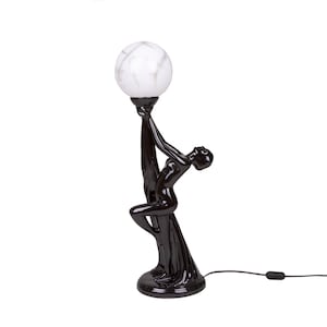 Op de afbeelding: Een zwarte keramische tafellamp met een witte marmeren globe-kap. De lamp heeft een gestileerde vrouwelijke figuur die de globe vasthoudt.