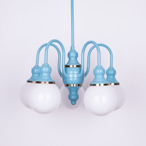 May include: A light blue chandelier with five white frosted glass globes. The chandelier has a gold trim around the base of each globe and the center of the fixture.