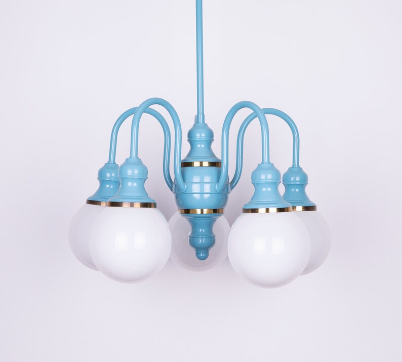 May include: A light blue chandelier with five white frosted glass globes. The chandelier has a gold trim around the base of each globe and the center of the fixture.
