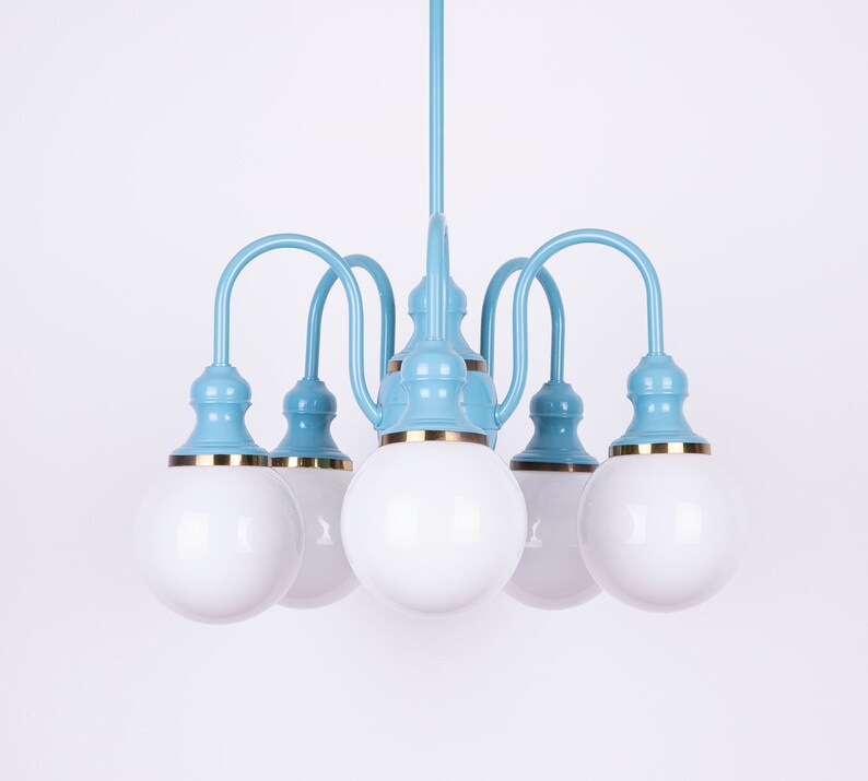 May include: A light blue chandelier with five white globe-shaped light bulbs. The chandelier has a gold trim around the base of each bulb.