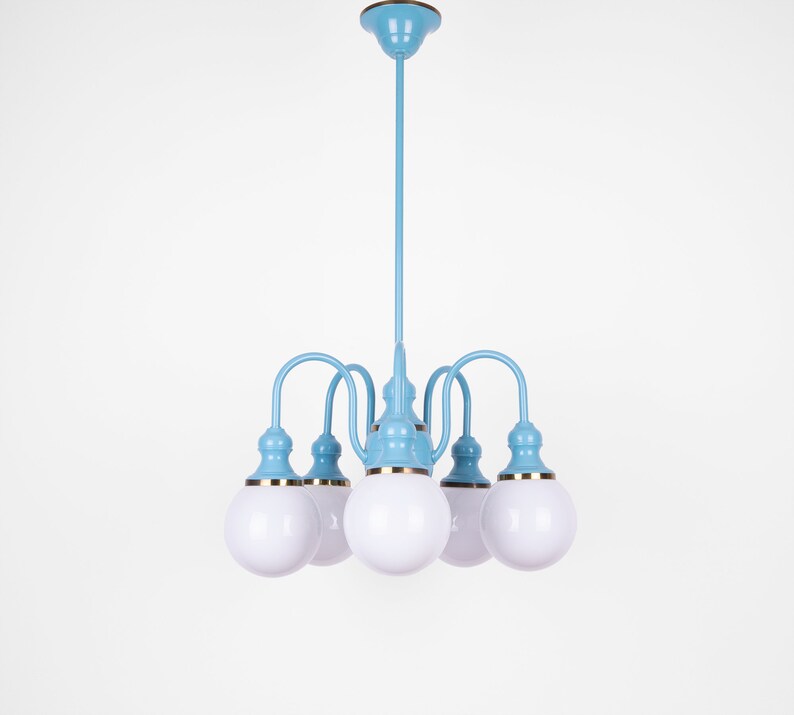 May include: A light blue chandelier with five white globe-shaped light bulbs. The chandelier has a gold trim around the base of each bulb.