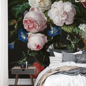May include: A floral wall mural featuring a classic still life of large, blooming roses in shades of pink and white, with accents of blue and yellow. The dark background enhances the vibrant colors of the flowers. A nightstand and bedding are in the foreground.
