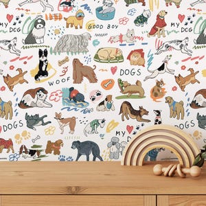 Pode incluir: Um arco-íris de madeira e uma chocalho para bebé estão numa superfície de madeira em frente a um papel de parede com um padrão repetido de cães ilustrados, pegadas e as palavras "WOOF", "DOGS" e "GOOD BOY". O papel de parede tem um fundo branco.