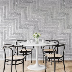 May include: A white round pedestal table with four black bentwood chairs featuring woven cane seats. The table holds a clear glass vase with white flowers. The background is a wall covered in wallpaper with a gray and white herringbone pattern.