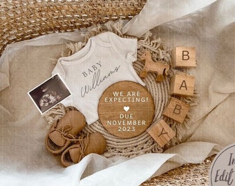 May include: A white onesie with the text "Baby Williams" on it, a wooden sign that says "We are expecting! Due November 2023", a wooden toy horse, and wooden blocks that spell out "Baby".